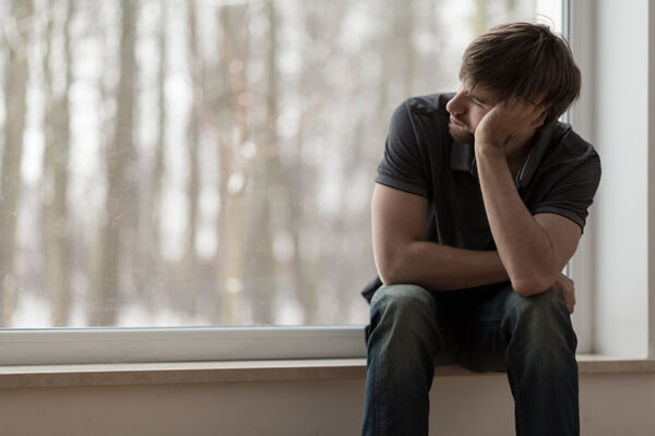 A man struggling with substance abuse sits and looks out the window.